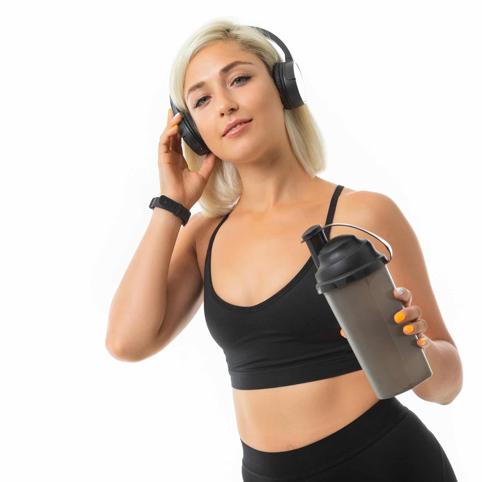 Sport caucasian blonde girl with earphones do sports and drinks water from sport bottle